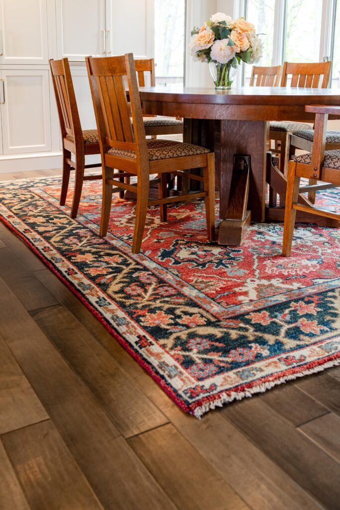 A dining room with a table and chairs and a rug on the floor.