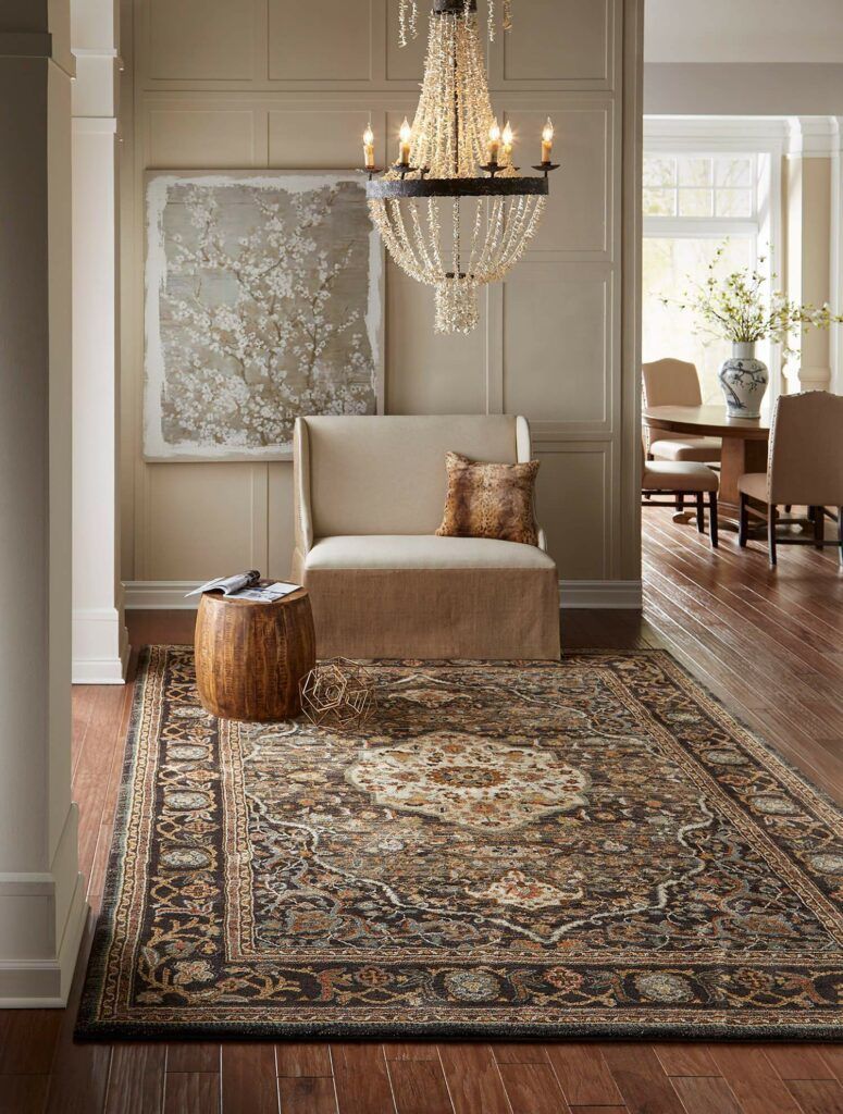 A living room with a rug , chair and chandelier.
