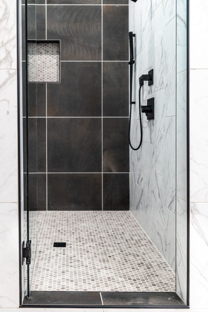 A walk in shower with black and white tiles and a glass door.