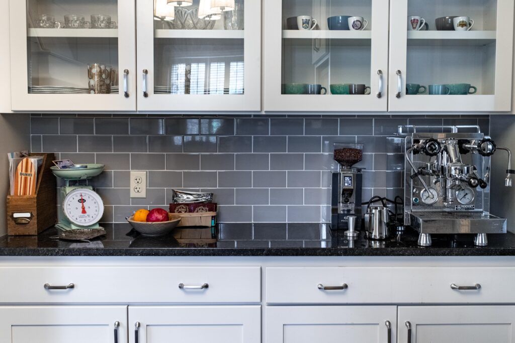 A kitchen with white cabinets , black counter tops , a scale and a coffee maker.