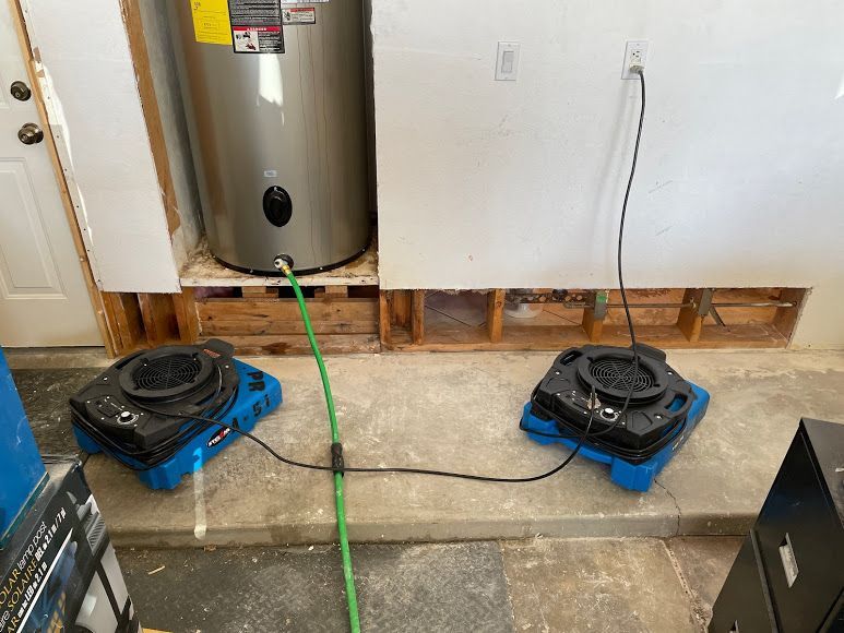 Two box fans on the floor beside a water heater and wall opening in a basement or utility room.