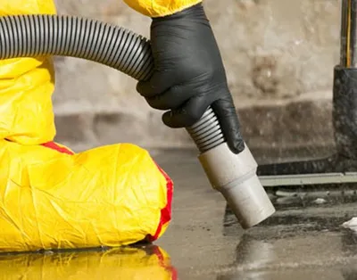 Worker in yellow protective suit uses a hose nozzle to clean a wet concrete floor.