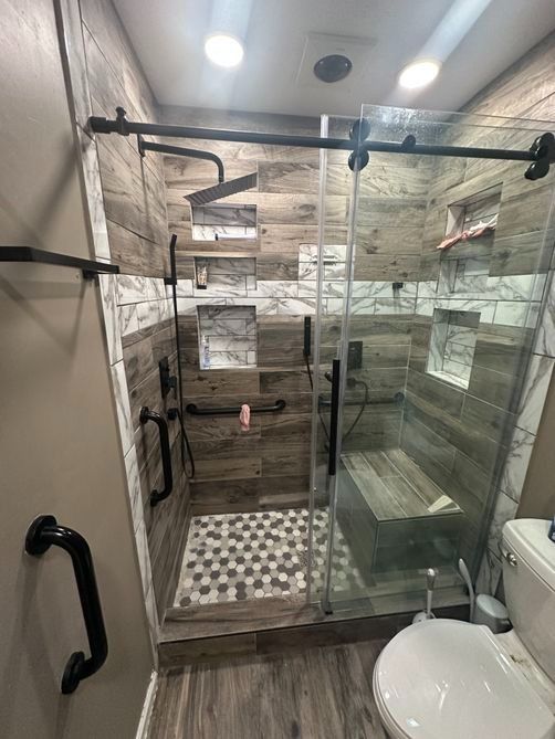 Accessible bathroom with glass walk-in shower, black grab bars, and toilet beside it