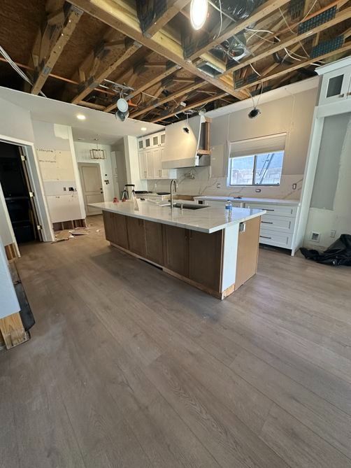 Open-concept kitchen with wood floors, island, white cabinets, exposed beams, and large window