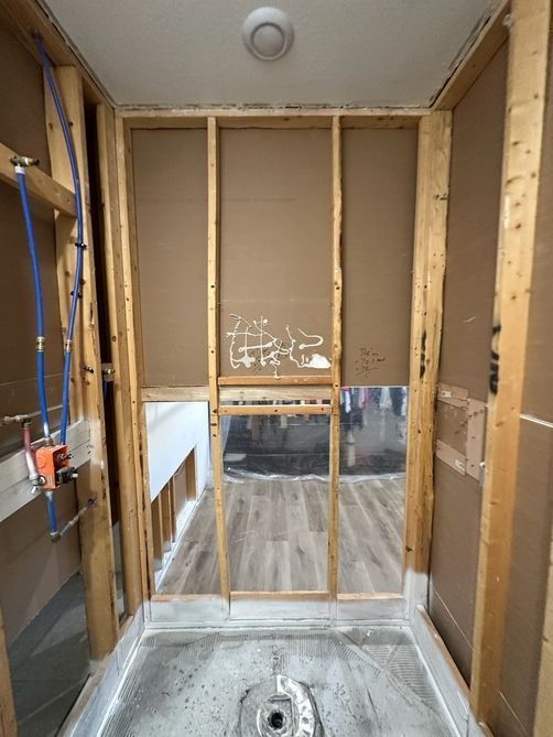 Empty bathroom framed for renovation, with exposed studs, shower plumbing, and a bare toilet drain.
