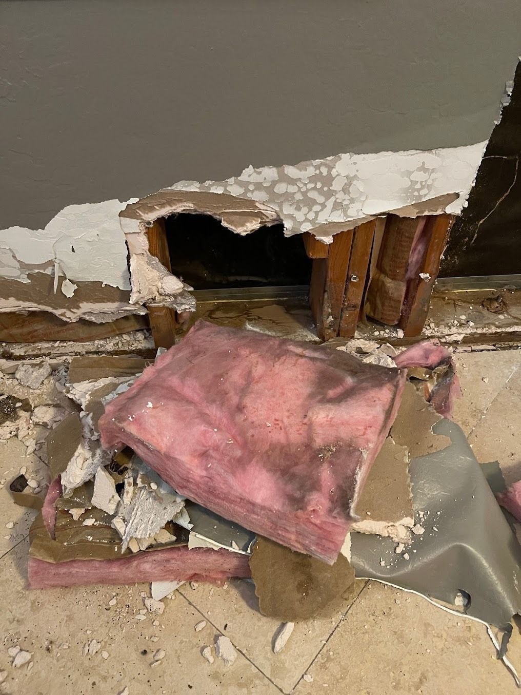 Damaged wall with a broken hole near the floor, debris, and a pink cushion on the ground.