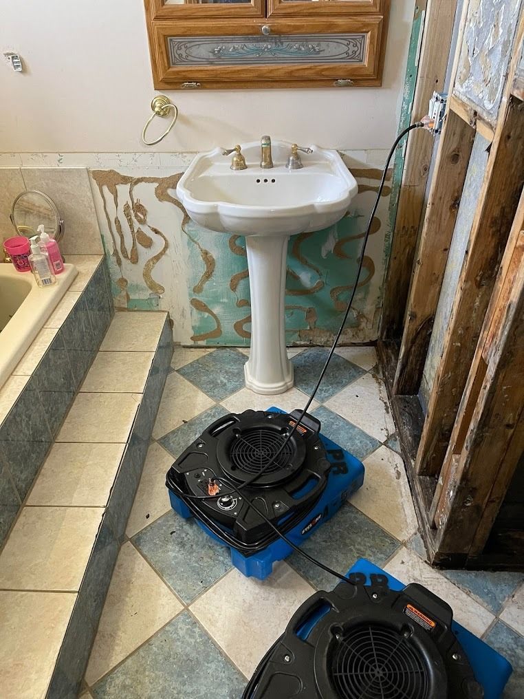 Bathroom with a pedestal sink and two fans on the tiled floor near a partially renovated wall