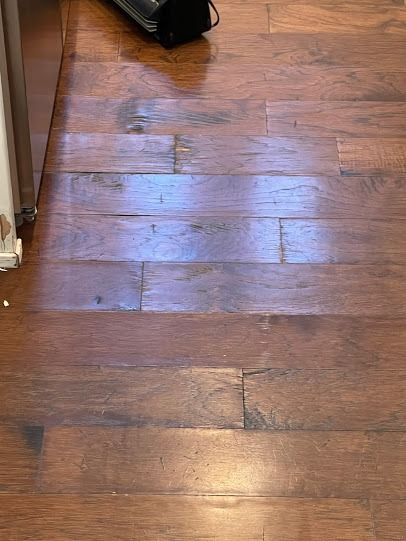 Wooden floor with sunlight reflection, a baseboard at left, and a black object near the top edge