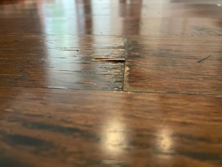 Close-up of a scratched wooden floor with a visible crack and reflected light.