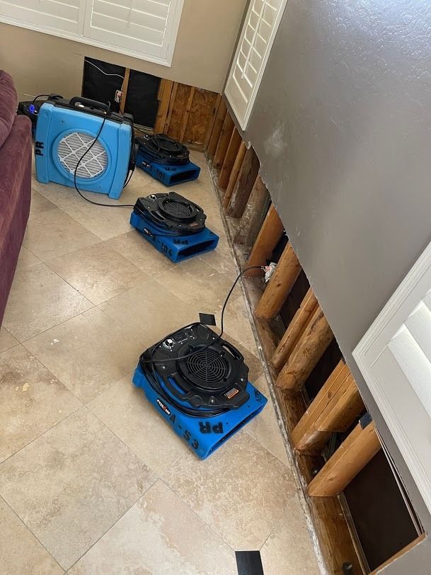 Blue floor fans set up in a hallway with exposed wall studs and beige tile floor.