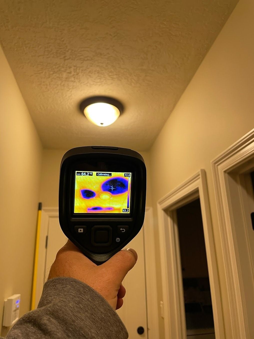 Handheld thermal camera aimed at a hallway ceiling light, showing a heat map on its screen