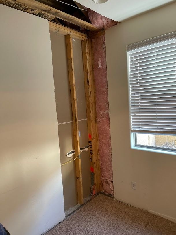 Partially demolished room with exposed wall studs, insulation, and a window with blinds