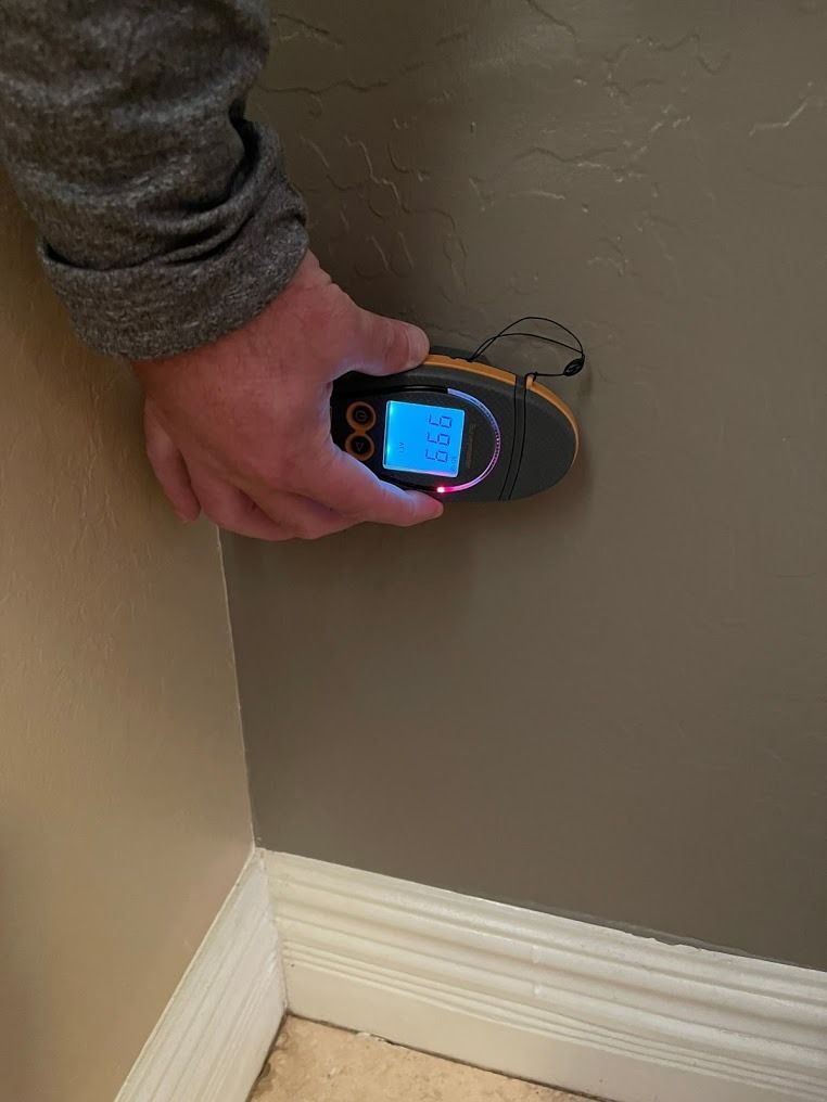 Hand holding a digital wall scanner against a beige wall near the baseboard.