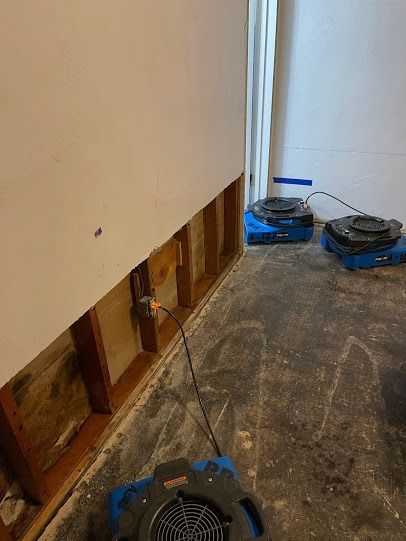 Unfinished room with exposed wall studs, construction debris, and a robot vacuum on the floor.