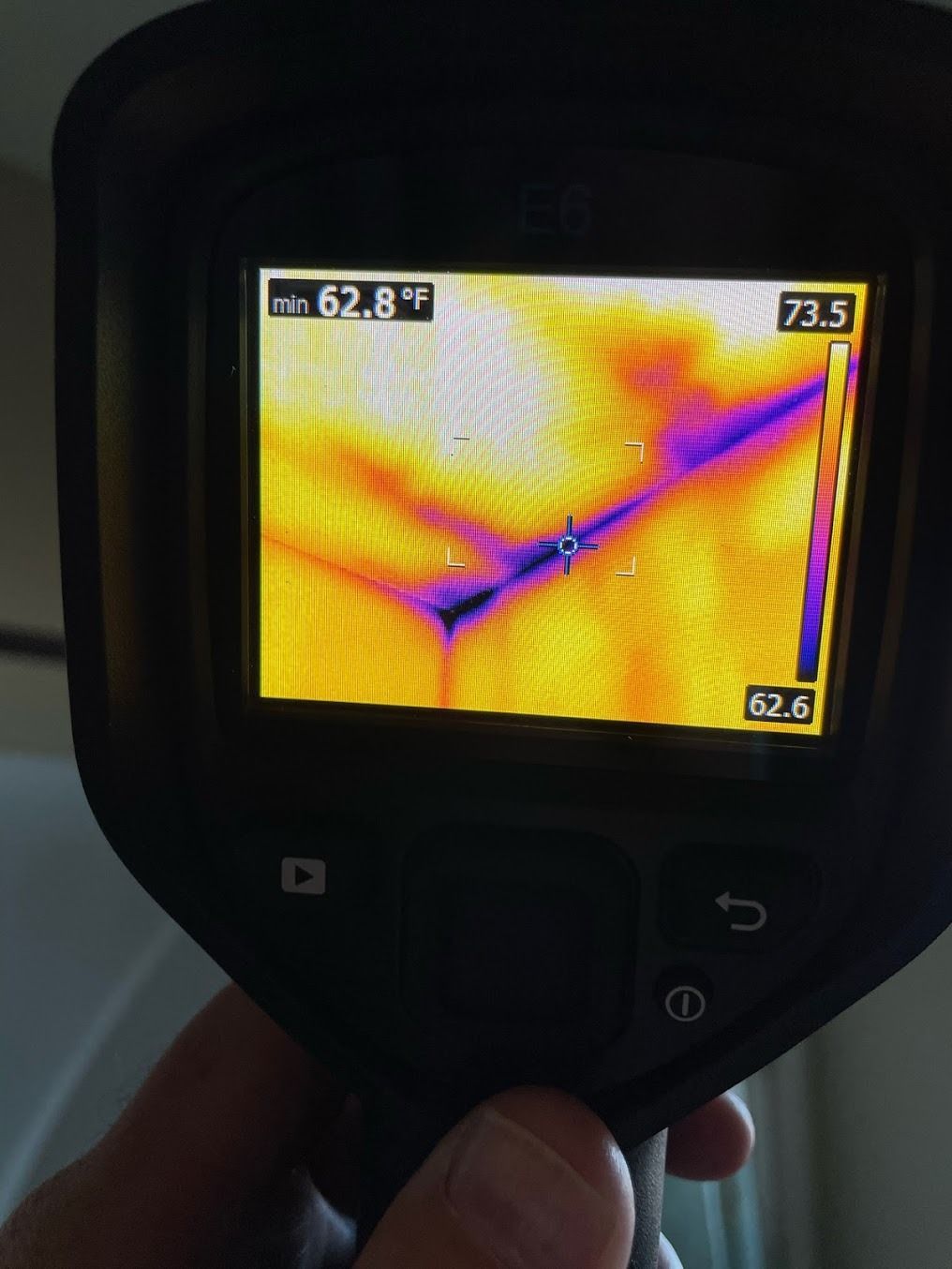 Handheld thermal camera showing a colorful heat map with a diagonal blue line and temperature readings.