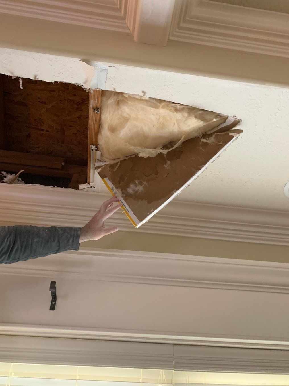 Ceiling panel torn open, exposing insulation, with a person holding the damaged section aside.