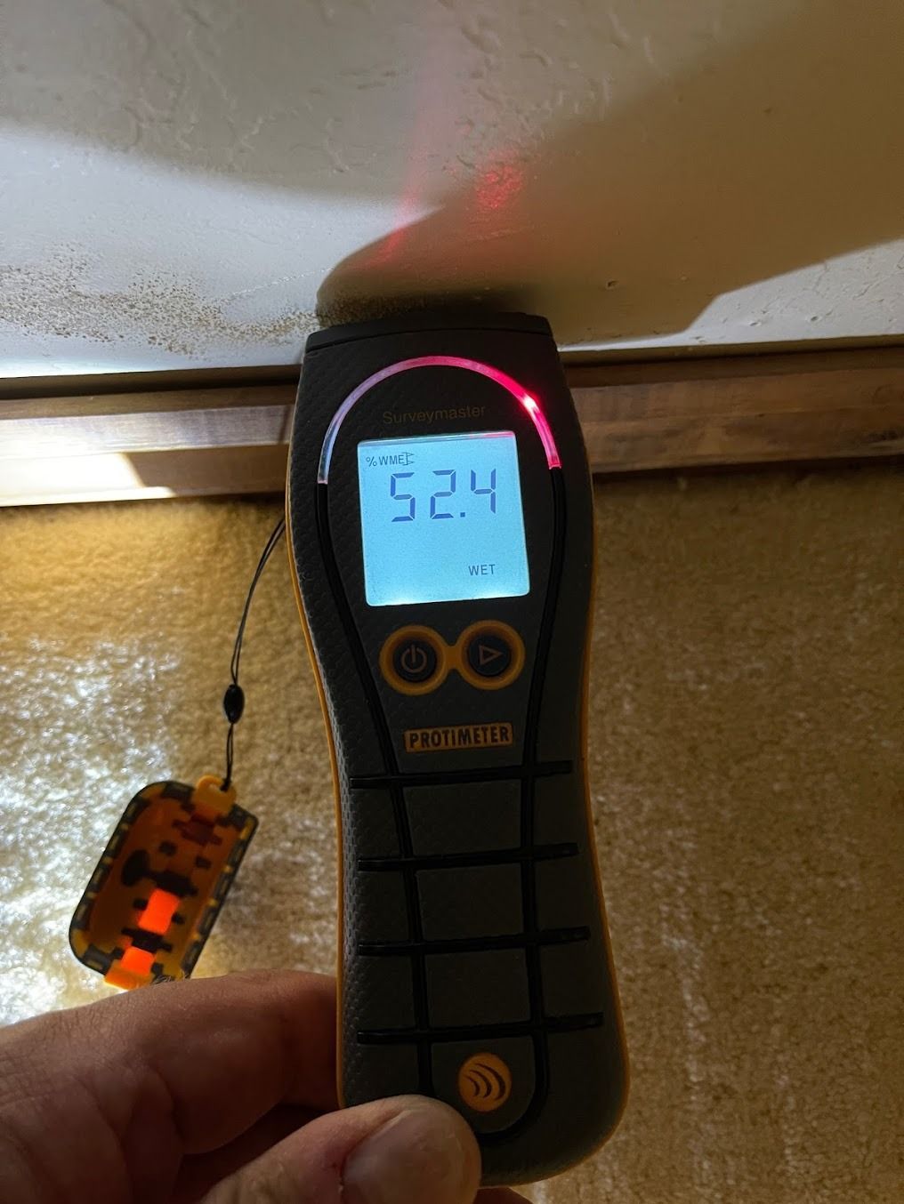 Handheld digital meter near a wall shows 52.4 with a glowing red display indicator
