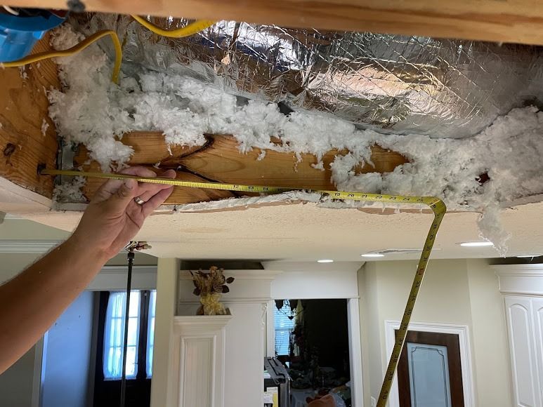 Hand holding a drop ceiling tile under exposed insulation and ductwork in a damaged room