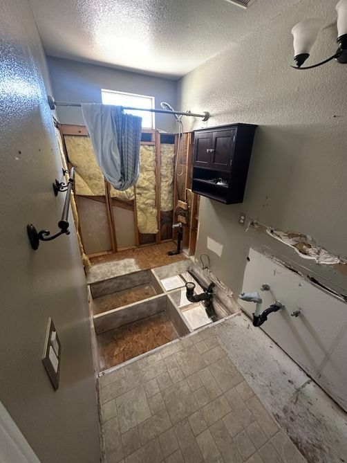 Damaged bathroom with broken tile, exposed wall, and curtained shower under repair