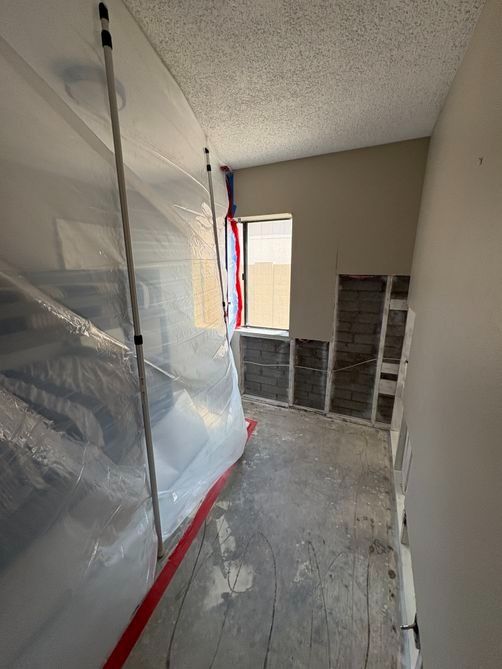Plastic sheeting and red tape cover a room under renovation near a window and stacked tiles.