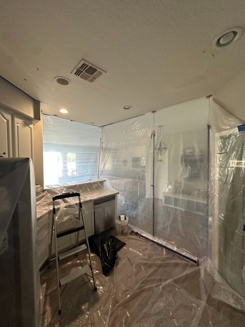Plastic-covered room under renovation with ladder, workbench, and window blinds in a home interior