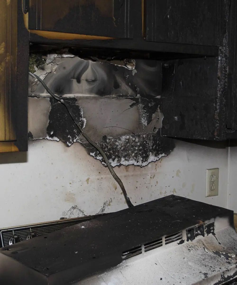 Charred kitchen wall and cabinets above a damaged stovetop with soot and smoke stains