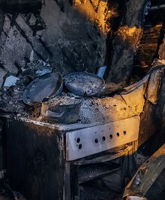 Charred stove with burned cookware amid fire-damaged debris and soot-covered walls