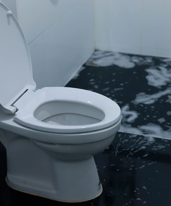 White toilet in a bathroom with water spilled across the dark floor