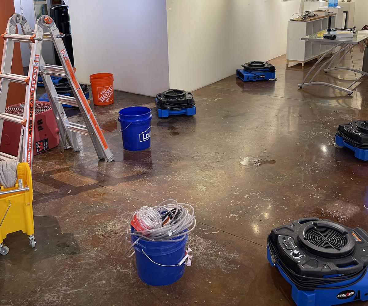 Wet room with cleaning supplies, buckets, and floor scrubber machines on a shiny concrete floor.