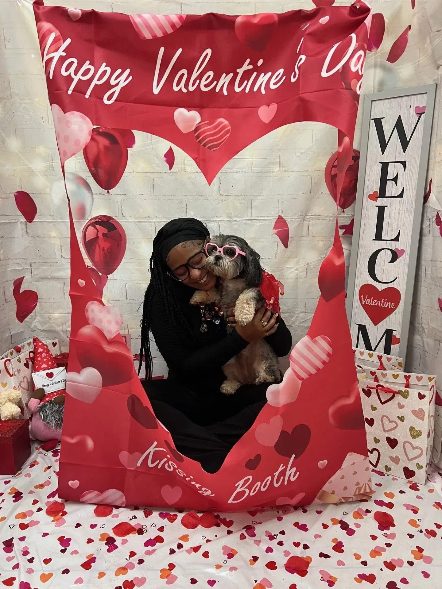 Woman holding a dog in a red Valentine’s Day photo booth with hearts and rose petals