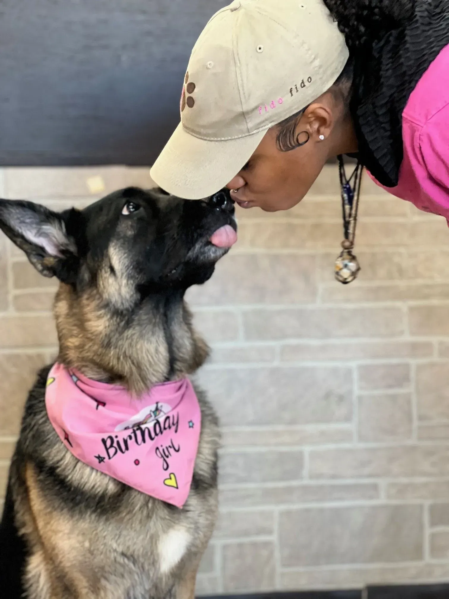 Woman leans in to touch noses with a German shepherd wearing a pink “Birthday Girl” bandana.