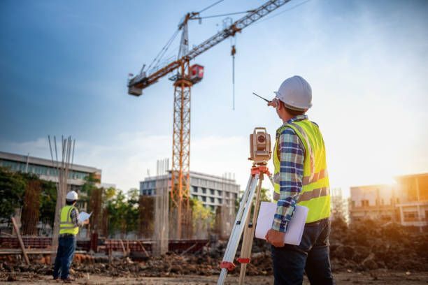Construction site workers surveying with instruments; crane and buildings in background
