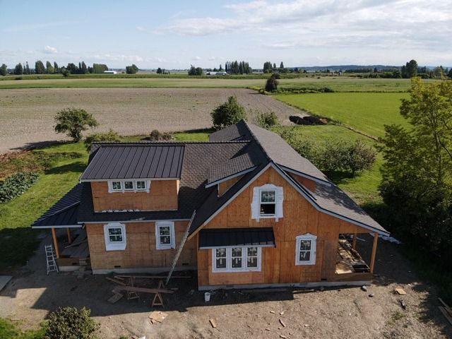 Wooden house under construction in a rural field with a dark metal roof.