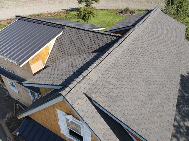 Overhead view of a house roof, with dark gray asphalt shingles and a section of black metal.