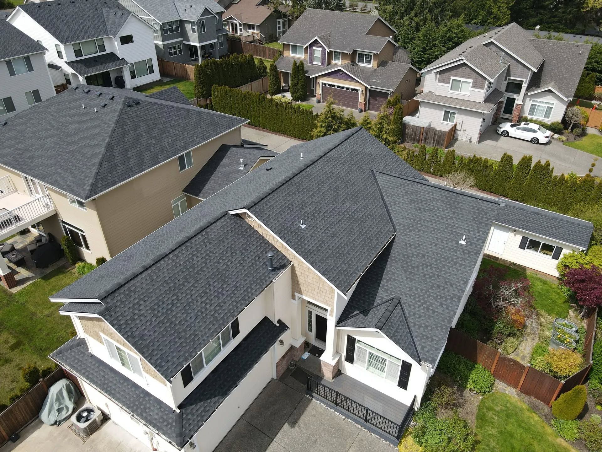 Aerial view of a suburban house with a dark gray roof. Other houses with similar architecture and greenery surround it.