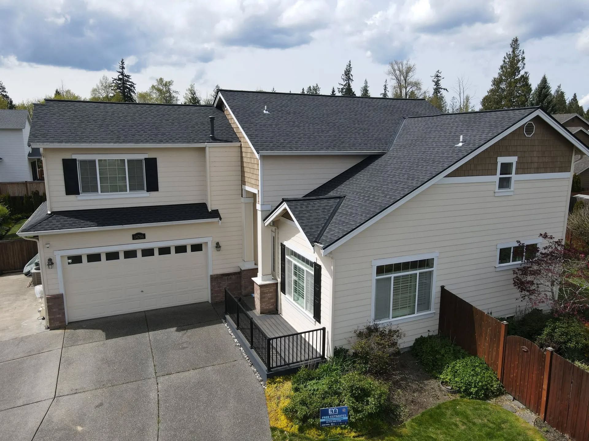 Two-story house with a black roof, beige siding, and a concrete driveway.