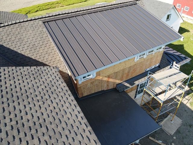 Overhead view of a house with a dark gray metal roof addition next to a dark shingle roof.
