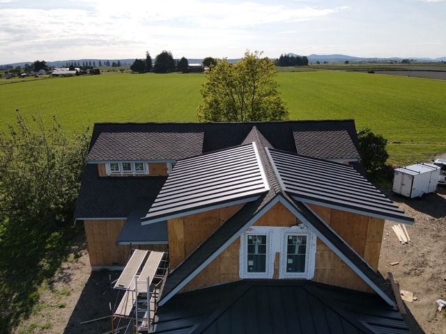 Partially constructed house with dark roof against a green field backdrop.