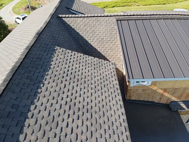 Overhead view of a house roof with asphalt shingles and a flat, dark metal section.