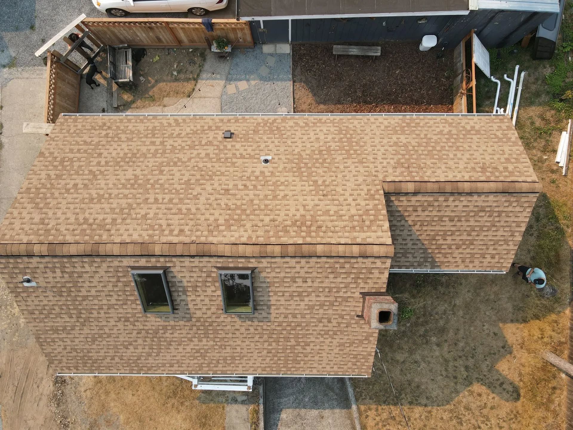 Overhead view of a house with a brown shingled roof, windows, and a small yard with fences.