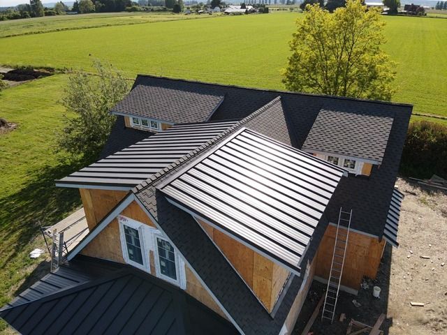 Black metal roof on a partially built wooden house, set in a field.
