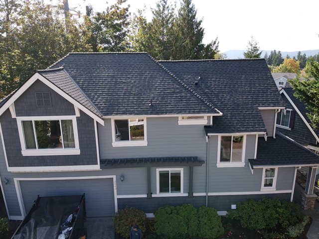 Two-story house with dark gray roof and siding, white trim, and a small garage, in a wooded area.