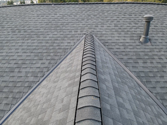 Gray shingle roof with a ridge, metal trim, and a vent pipe.