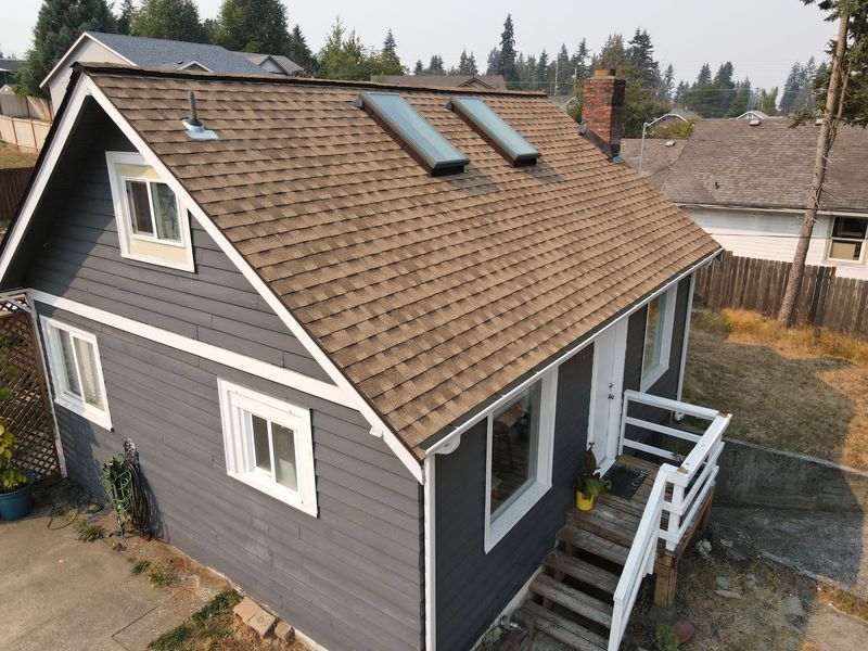 Gray house with brown roof, two skylights, and white trim. Wooden steps lead to a front door.
