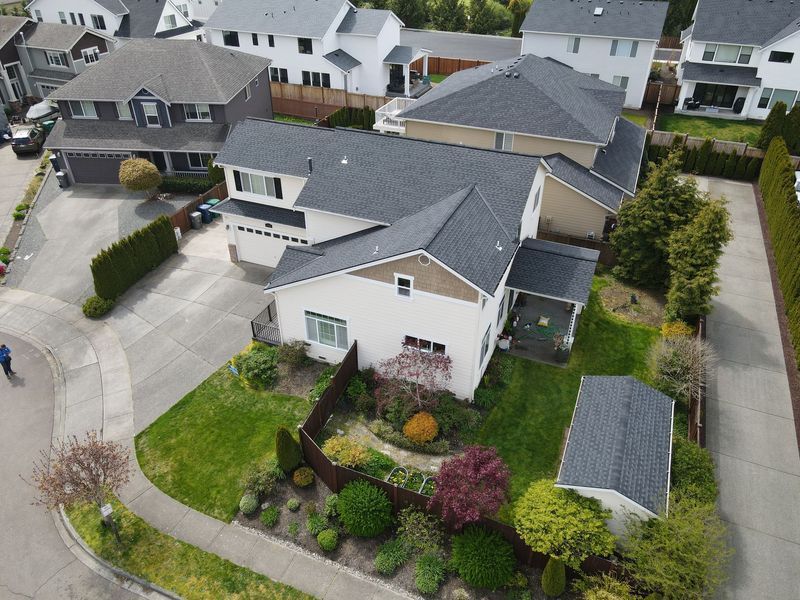 Aerial view of a two-story house with a grey roof, surrounded by green lawns and other houses.