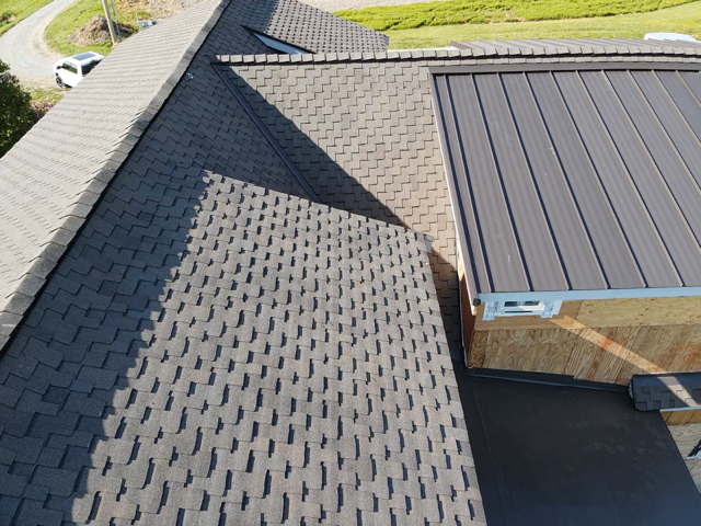 Overhead view of a house roof with asphalt shingles and a metal section, under a bright sky.