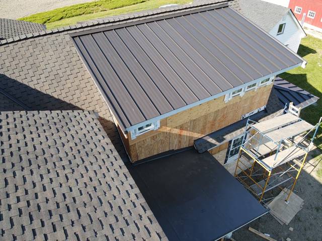 Overhead view of a house with a dark gray metal roof section and asphalt shingle roof.