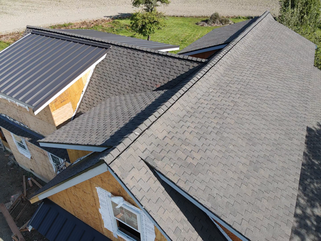Aerial view of a house under construction with a dark gray asphalt shingle roof and a dark gray metal roof section.
