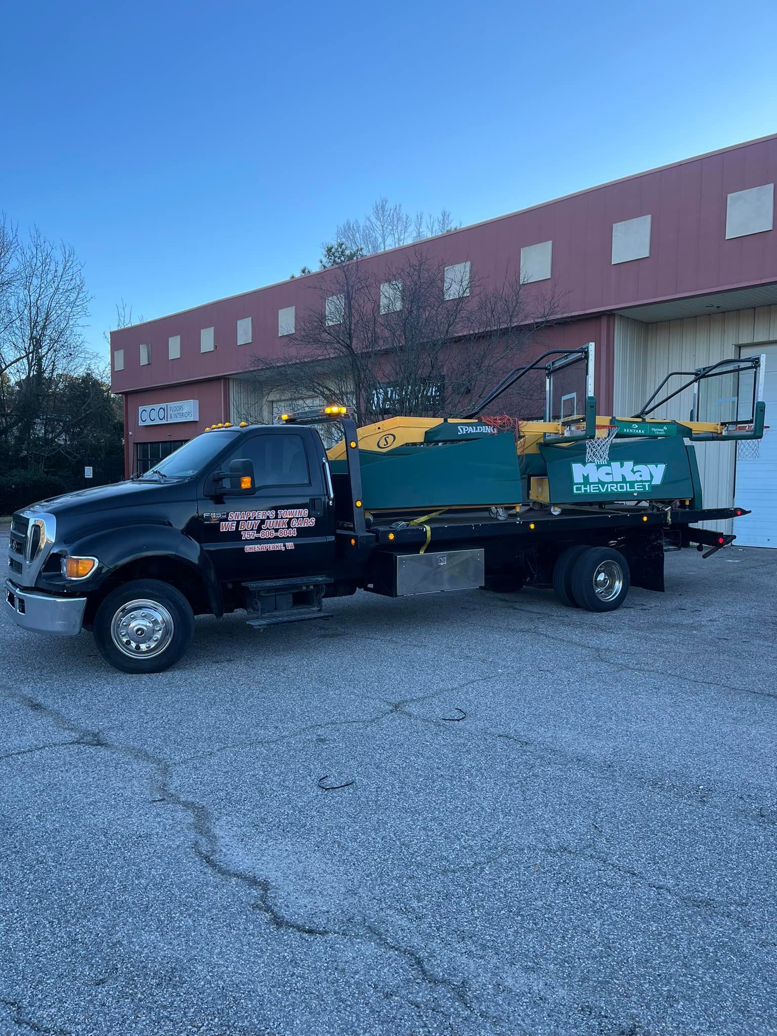 Black work truck with green and yellow equipment on the bed, parked in front of a red building.