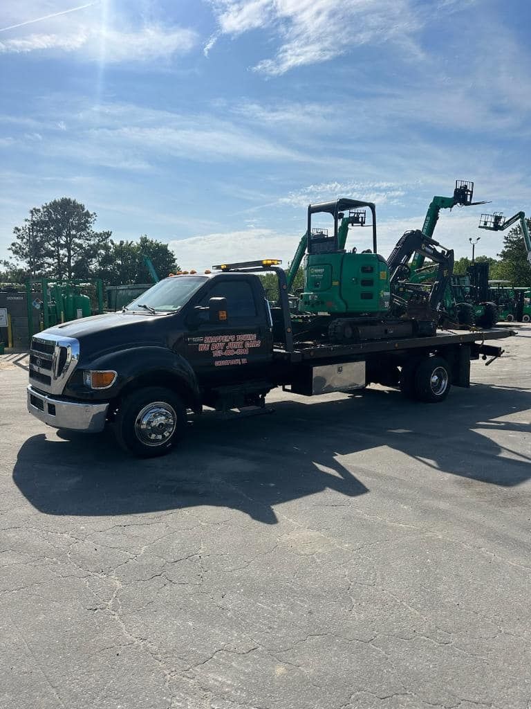 Black tow truck carrying a green construction machine on a sunny day.